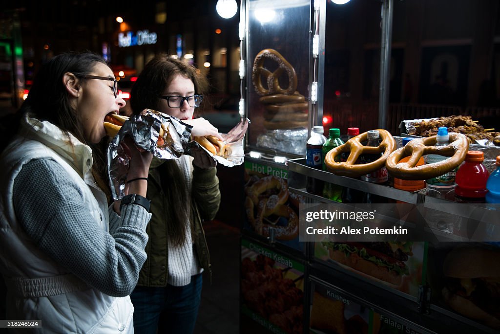 Two teenager girls, sisters, eats fastfood on the street