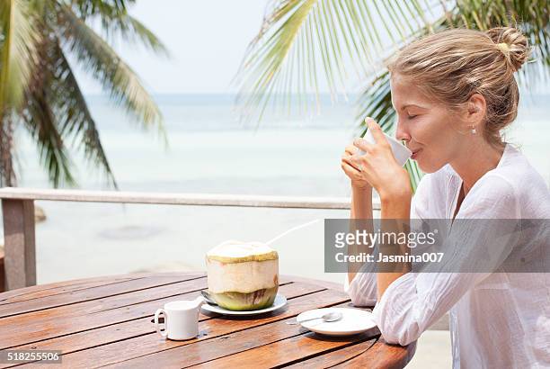 young woman enjoys drinking coffee and coconut - coconut beach woman stock pictures, royalty-free photos & images