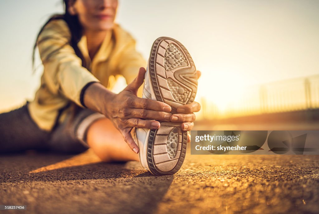 Close-up of woman stretching her leg at sunset.