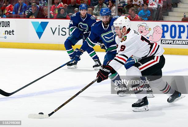 Chris Higgins of the Vancouver Canucks looks on as Jonathan Toews of the Chicago Blackhawks skates up ice with the puck during their NHL game at...