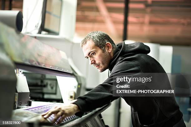male worker operating on industrial printer - printing industry stock pictures, royalty-free photos & images
