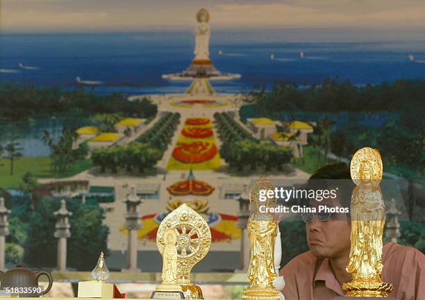 Chinese man sells souvenirs in front of a drawing of the soon to be constructed 108-metre-high statue of the South Sea Avalokitesvara, also known as...