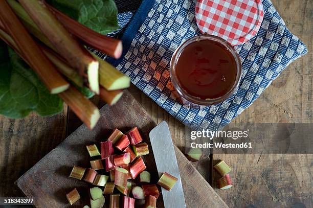 sliced and whole rhubarb and jam jar of rhubarb jelly on wood, elevated view - rabarber stockfoto's en -beelden