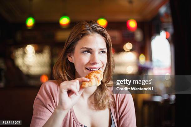 france, paris, portrait of happy young woman eating a croissant in a cafe - croissant stock-fotos und bilder