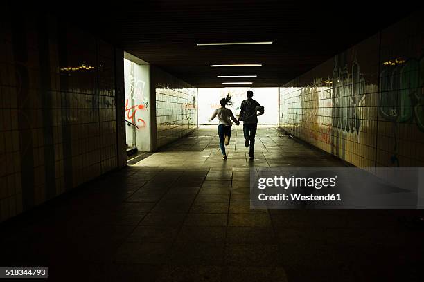 young couple running hand in hand in a dark underpass, partial view - dark background light stock-fotos und bilder