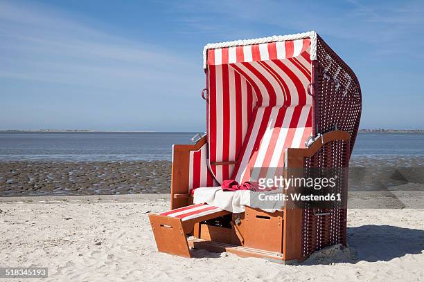germany, lower saxony, dornum, nessmersiel, red and white hooded beach chair - beach shelter stock-fotos und bilder