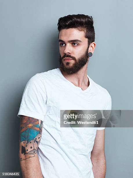 portrait of tattooed brunette man in front of gray background - looking away stock-fotos und bilder