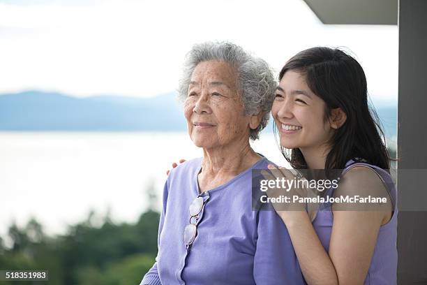 senior asian woman and granddaughter enjoying view from balcony - aziatische cultuur stockfoto's en -beelden