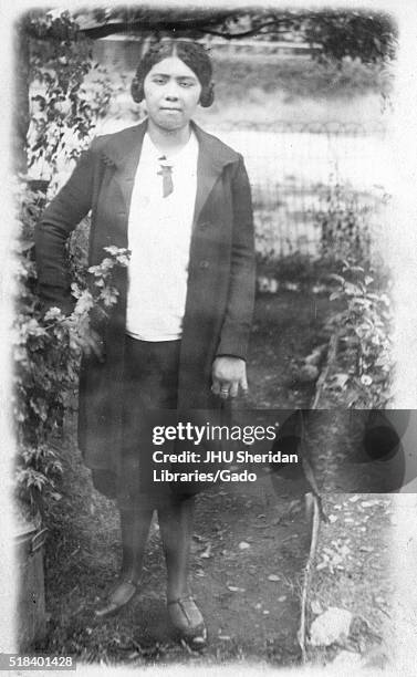 Portrait of an African American woman standing in front of a body of water, she is standing on dirt and to the left is shrubbery, she is wearing a...