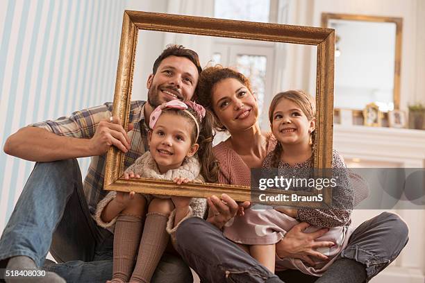 smiling family having fun with a picture frame at home. - family picture frame stockfoto's en -beelden