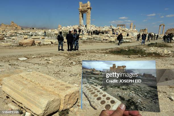 General view taken on March 31, 2016 shows a photographer holding his picture of the Temple of Bel taken on March 14, 2014 in front of the remains of...