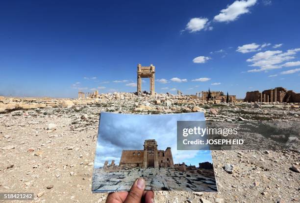 General view taken on March 31, 2016 shows a photographer holding his picture of the Temple of Bel taken on March 14, 2014 in front of the remains of...