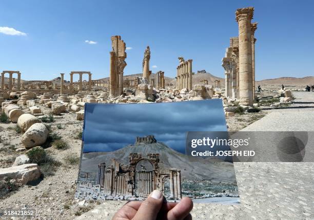 General view taken on March 31, 2016 shows a photographer holding his picture of the Arc du Triomphe taken on March 14, 2014 in front of the remains...