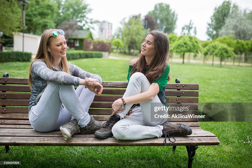 Happy friends communicating while relaxing on a bench outdoors.