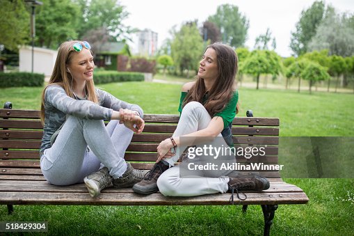 Happy friends communicating while relaxing on a bench outdoors. Happy friends communicating while relaxing on a bench outdoors.