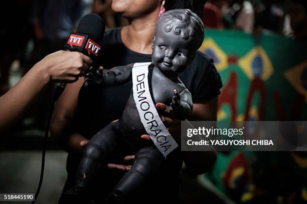 Supporter of Brazils Workers' Party speaks to a news TV channel an interview handing a doll during a demonstration in support of President Dilma...