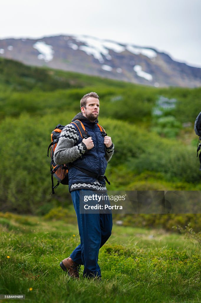 Hiker walking on grassy field against mountain