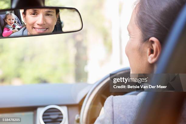 mother looks in backmirror at daughter in car. - rear view mirror stock pictures, royalty-free photos & images