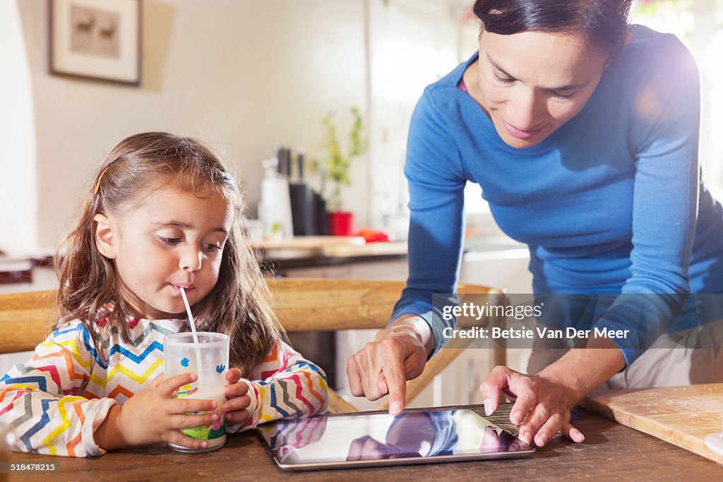 Child looks how mother uses digital tablet..