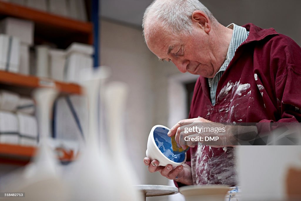 Senior potter painting a clay pot at workshop