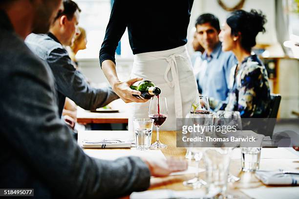 waitress pouring wine into glass at table - waitress foto e immagini stock