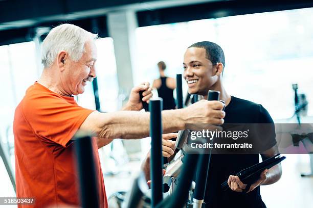 persönlicher trainer helfen senior mann in fitness - cross trainer stock-fotos und bilder