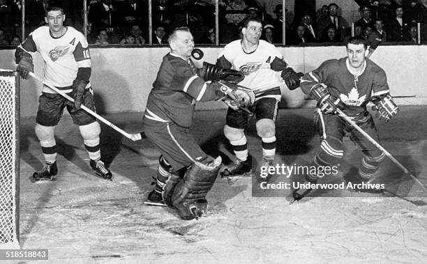 Toronto Maple Leaf goalie Johnny Bower appears to be stopping the puck with his chin in a National Hockey League game against the Detroit Red Wings,...