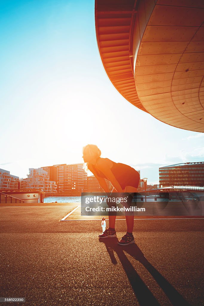 Tired female runner rests in the sunset with water bottle