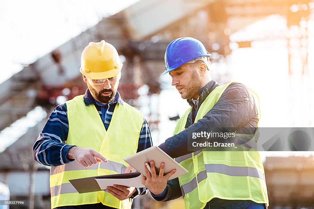 Engineer and construction site manager dealing with blueprints and budget