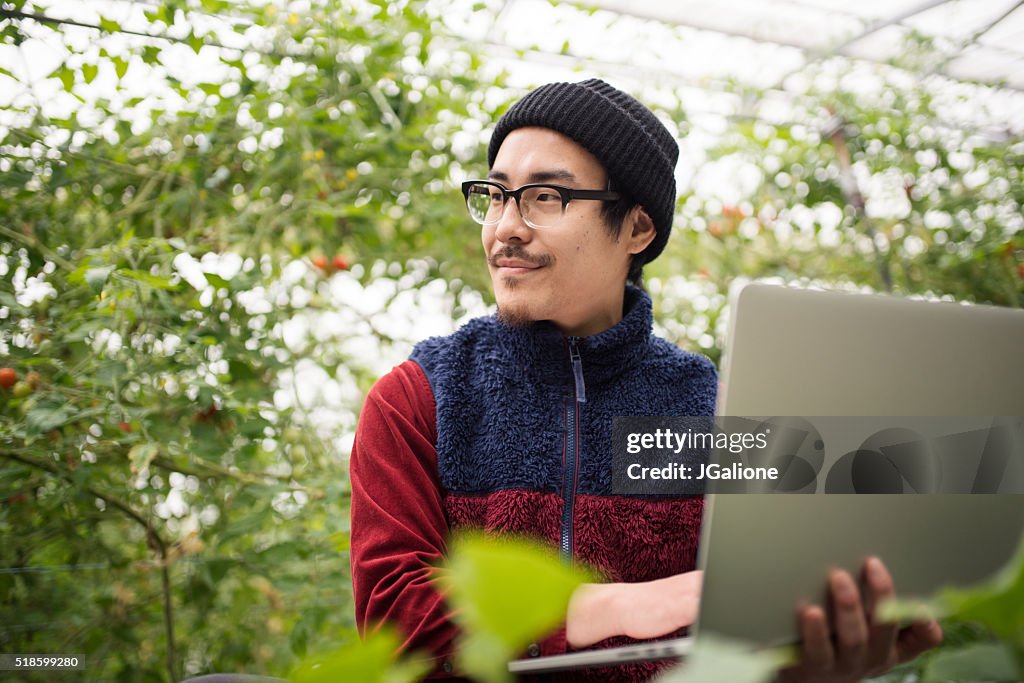 Farmer using laptop computer to conduct research in a greenhouse