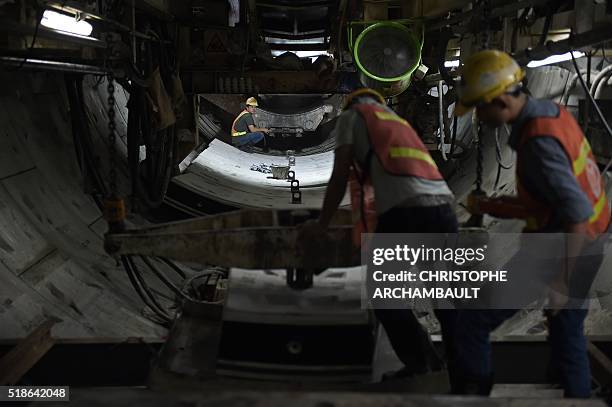 This picture taken on March 11, 2016 shows workers handling curved concrete segments to be attached to form the inner surface of a tunnel being dug...