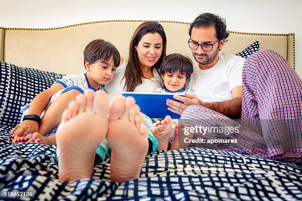spanier mit tablet mit eltern, ihre kinder auf dem bett - boy in pajamas and mom on tablet stock-fotos und bilder