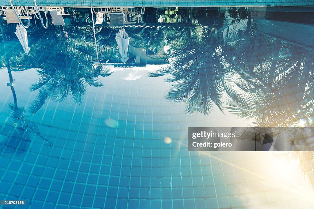 Reflection of sun and palm trees in blue swimming pool