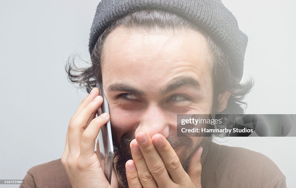 Smirking young man talking on phone over gray background