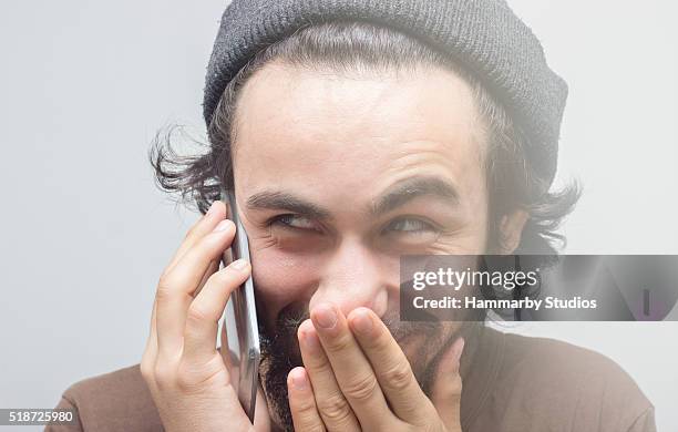 smirking young man talking on phone over gray background - liar stock pictures, royalty-free photos & images