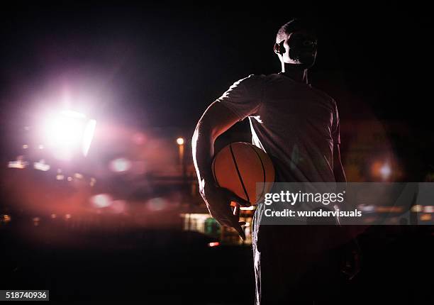 männliche basketball-spieler hält den kugel in den abend an der hüfte - african american male style stock-fotos und bilder