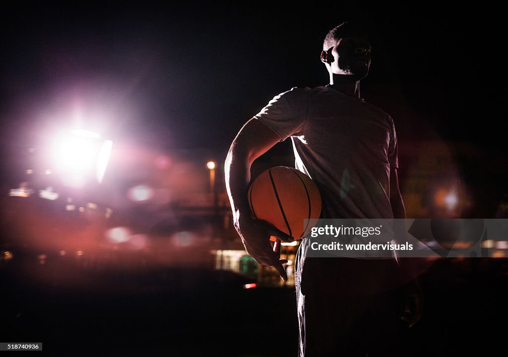 Male basketball Player Holding ball on hip in Evening