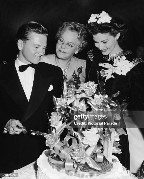 American actor Mickey Rooney wears a tuxedo and cuts his 21st birthday cake as his mother Nell Yule and girlfriend American actress Ava Gardner look...