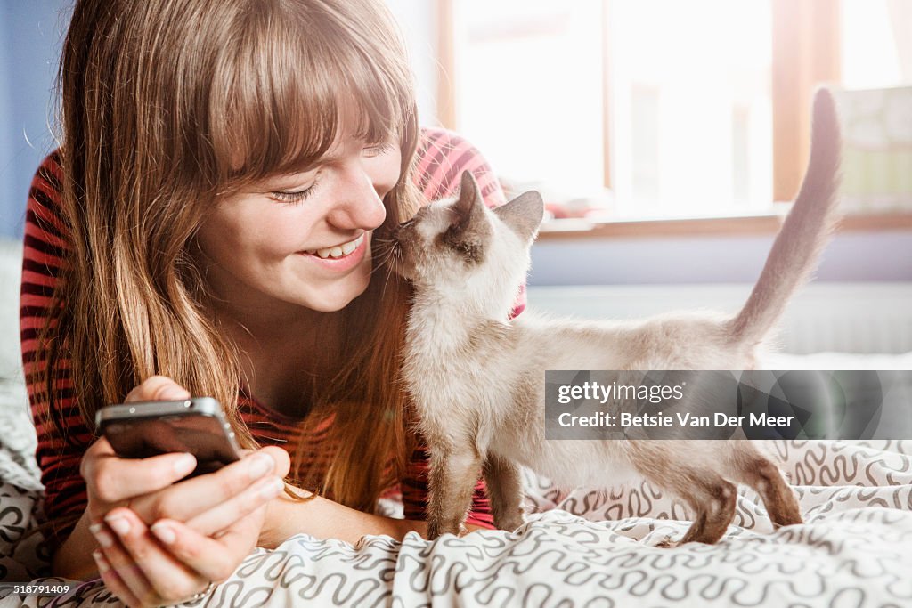 Young woman with phone gets cuddles from kitten.