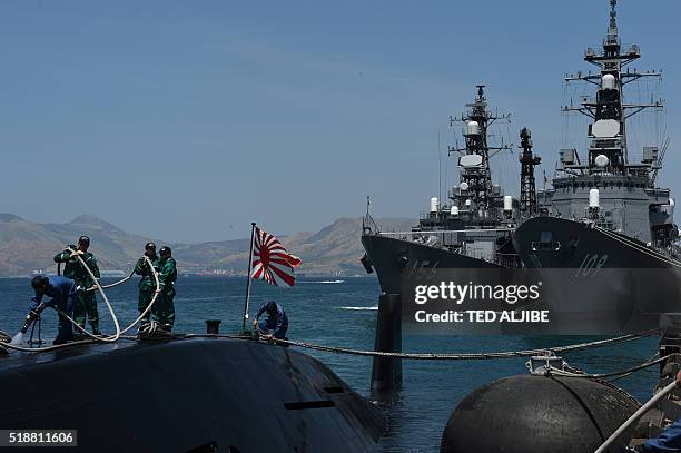 Crew members of Japanese submarine Oyashio work on the deck while Japanese destroyers JS Ariake and JS Setogiri dock at a port of the former US naval...