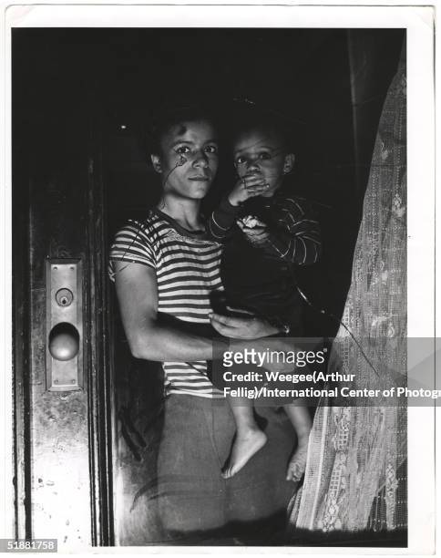 Mother holds her child in a window, Harlem, New York, New York, 1943. 'This tragic picture is of that evil thing, race hatred. Mrs. Bernice Lythcott...