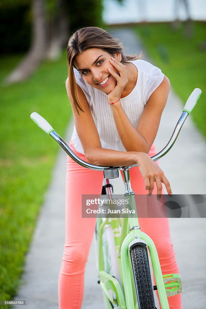 Young woman standing on bicycle outdoors smiling