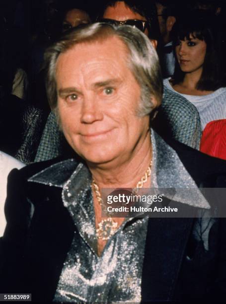 Portrait of American country music vocalist George Jones seated at an unidentified event, late 1980s. He is dressed in a black jacket with a leaf...