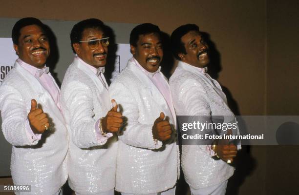 The Four Tops, dressed in matching, sequinned white tuxedos, pink shirts, and white bow ties, give the thumbs up backstage at an unidentified event,...