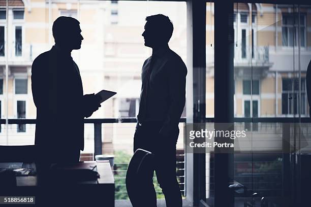 silhouette businessmen discussing in dark office - 2 businessmen in silhouette stock pictures, royalty-free photos & images