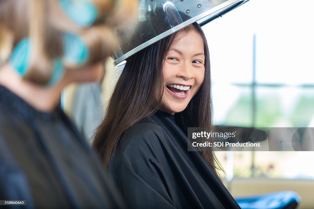 Asiática mujer sentada en un secador de cabello en el salón de belleza