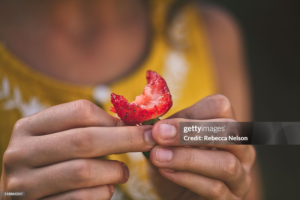 Girl holding strawberry with a bite out of it