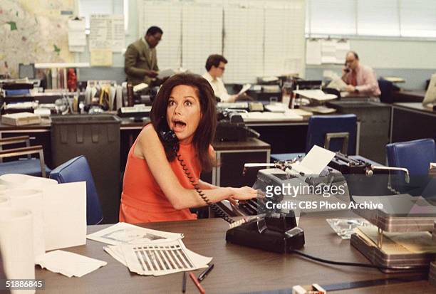 American actress Mary Tyler Moore mouths surprise on the telephone while simultaneously typing as others work in the background in a scene from 'The...