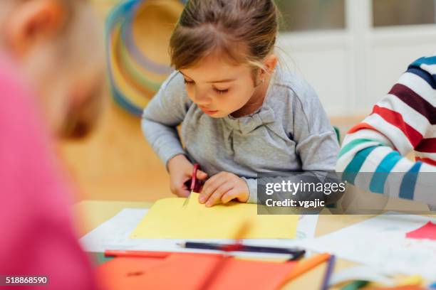 happy little girl using scissors in kindergarten. - nursery school building stock pictures, royalty-free photos & images