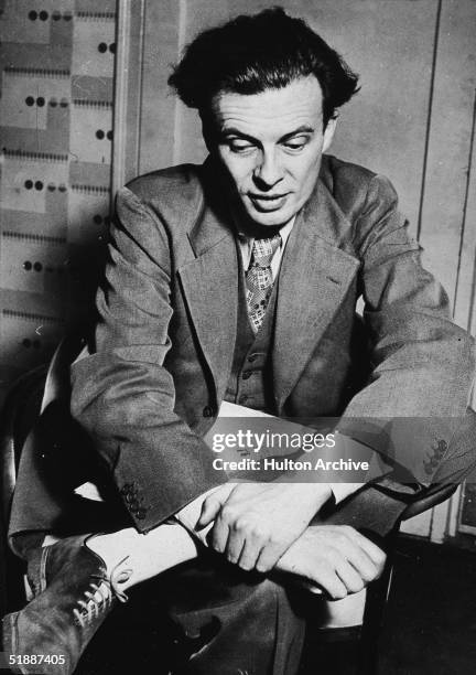 British writer Aldous Huxley sits with a newspaper on his lap, 1930s.